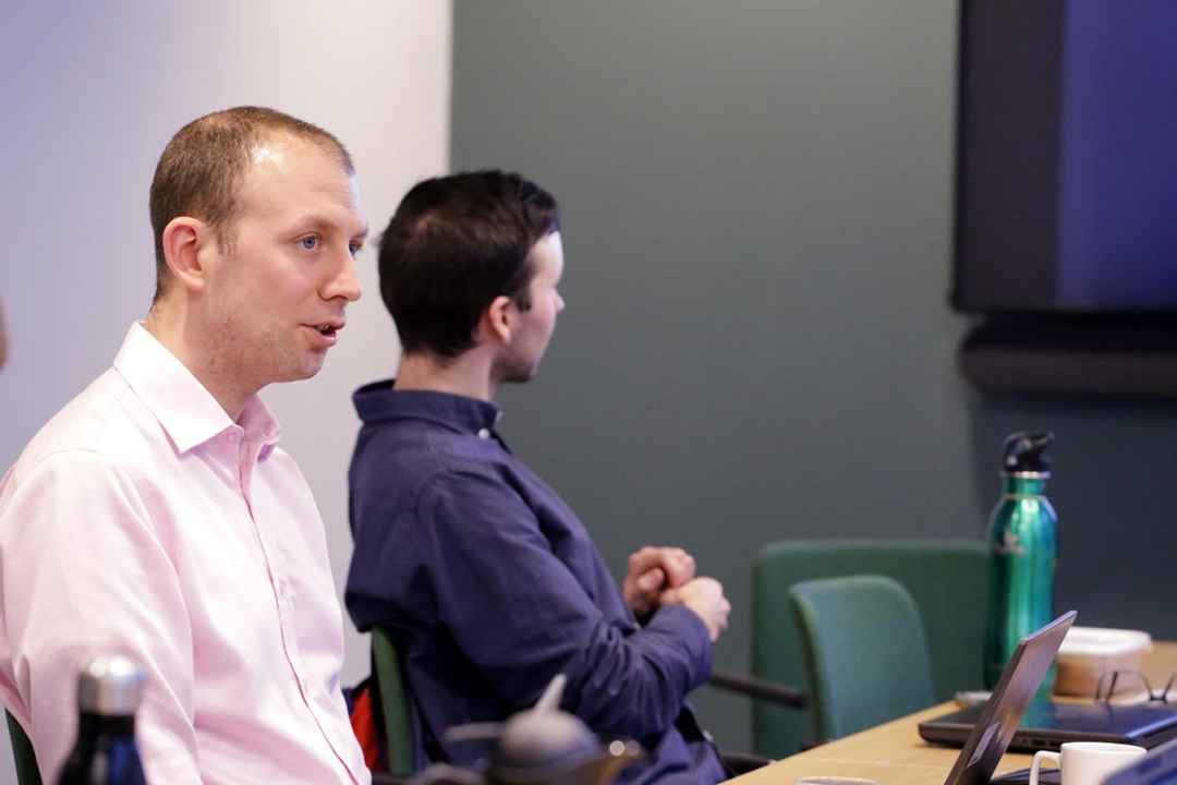 A person giving a presentation next to a conference room table.